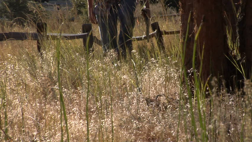 This is a slow motion shot of a man walking in a field with a gun in his hand.  Great as a murder reenactment shot, or a flash back, etc.