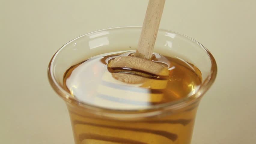 Honey twirler is dipped into a glass of honey and lifted.	