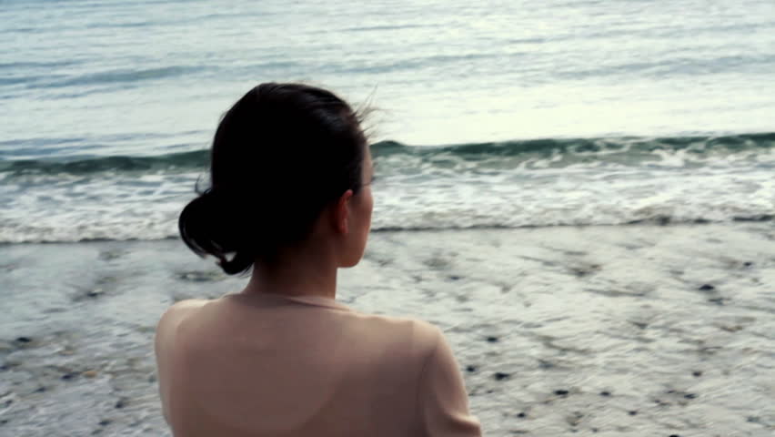 Young woman thoughtfully looking out to sea, camera stabilizer shot 