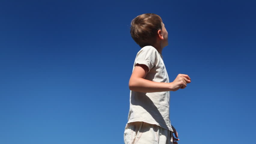 boy turns, says and looks showing his hand up against blue sky in clear sunny day