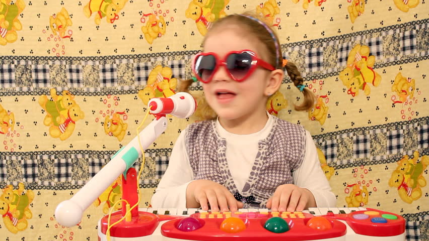 little girl plays toy piano and sings into a microphone 