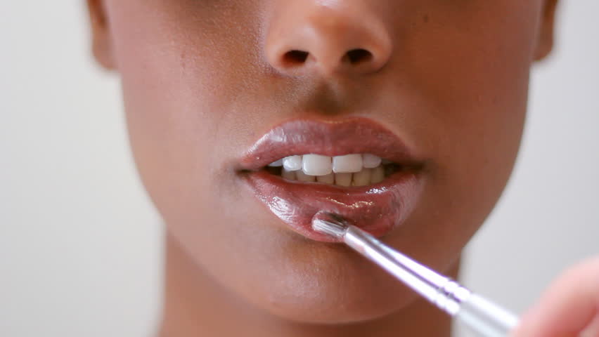 Lip gloss. Makeup artist uses brush to apply lip gloss to model's lips.  Shallow depth of field. 