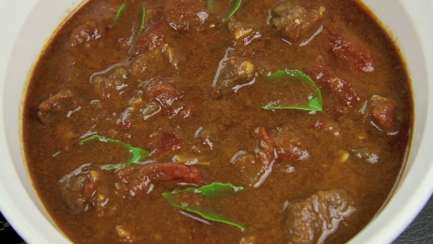 Close up of a serving spoon being dipped into an Indian curry.