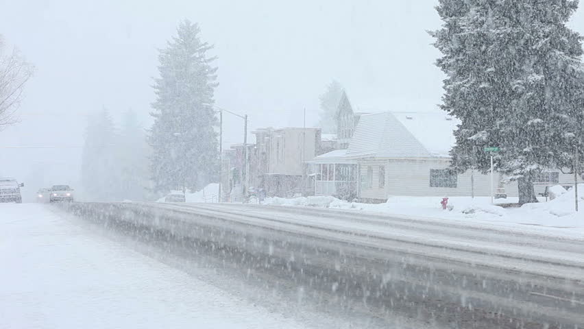 Storm snow blizzard small rural town with cars drive through heavy snow blizzard in late winter on main street of a small country town. City center with old pioneer businesses.