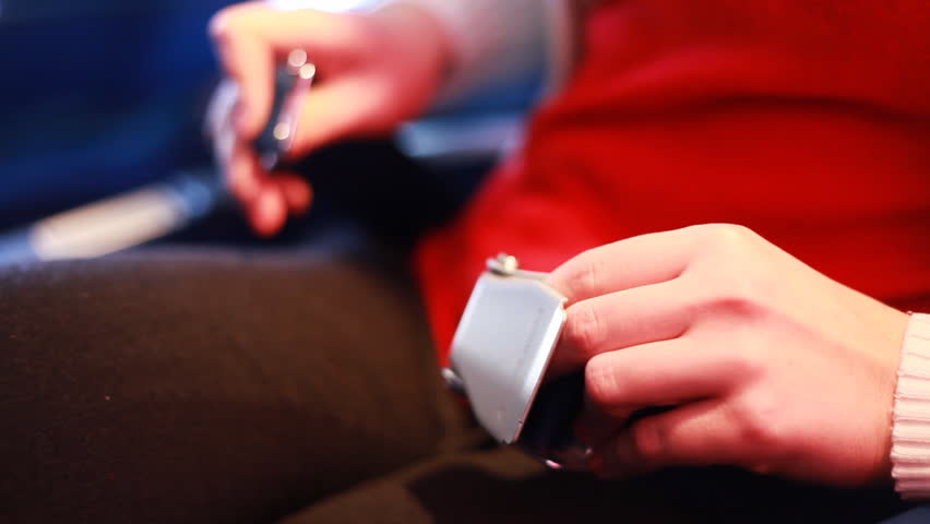 hands of girl sitting in passenger chair, buttoning seatbelt before airplane takeoff 