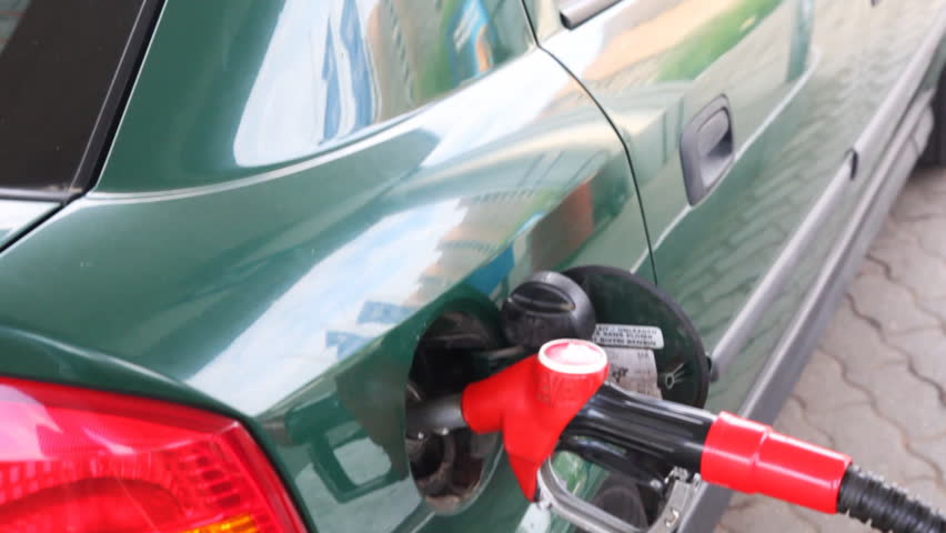passenger car in dark-green on petrol station, close-up red filling pistol, inserted into neck of tank