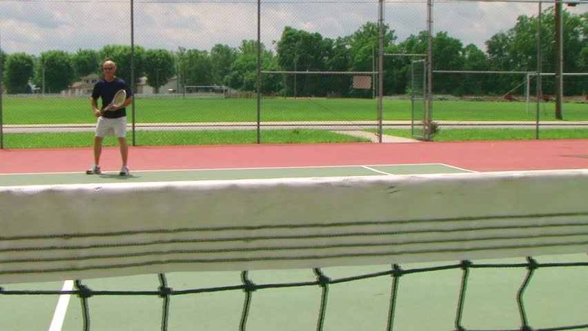 Tennis player volleys using forehand technique, crane shot across net. 