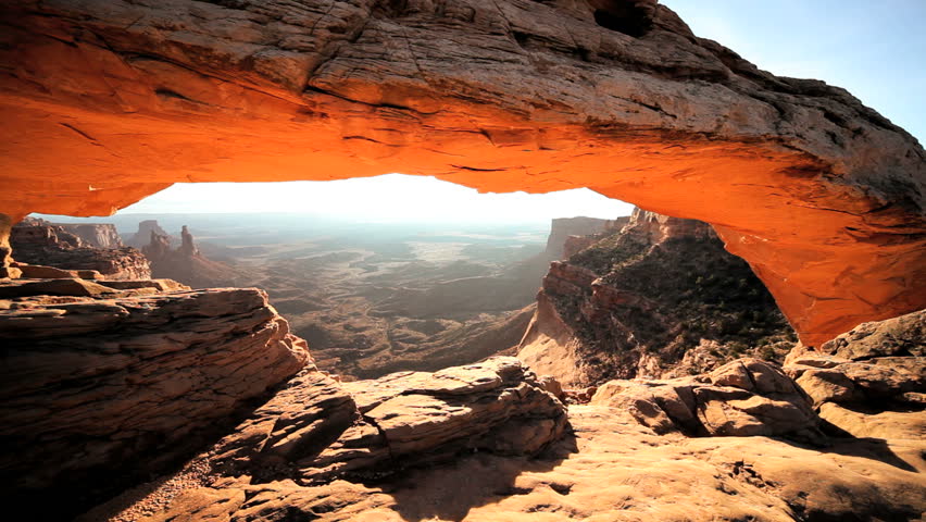 Panoramic view of a desert landscape through the sunrise hitting the sandstone Mesa Arch in Utah