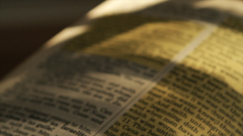 The camera pans across the text of a Bible and rests on chapter 3 verse 16 of the book of John.