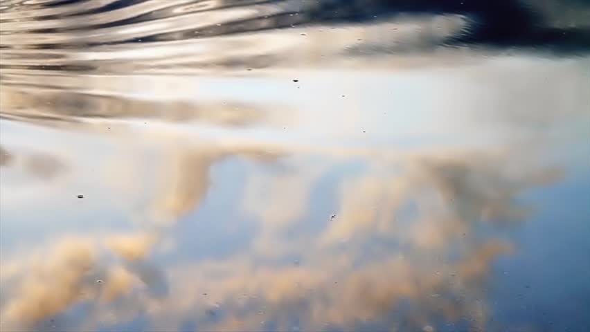 Clouds, golden from the setting sun, and blue sky reflected in a tidal pool with periodic waves washing over and through. Looping 1920x1080p.