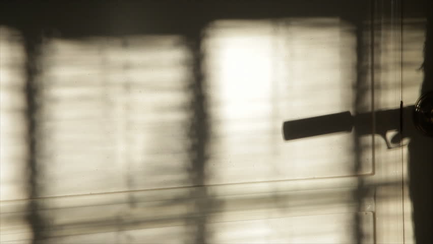 The evening or morning sunlight through window blinds captures the silhouetted firing of a pistol with a silencer attached to it. Blaze and smoke added to gun action in post.