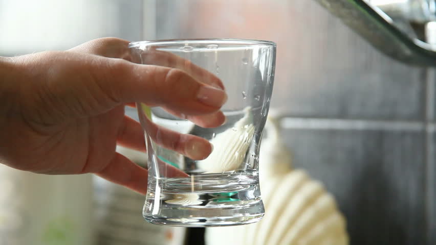 closeup of a female hand, pouring water in glass, from kitchen tap.