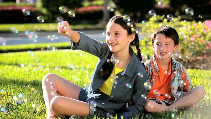 Two caucasian children in their garden laughing at play bubbles