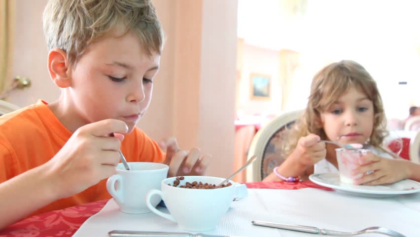 Boy and girl with curly hair eat granola and yogurt for breakfast 