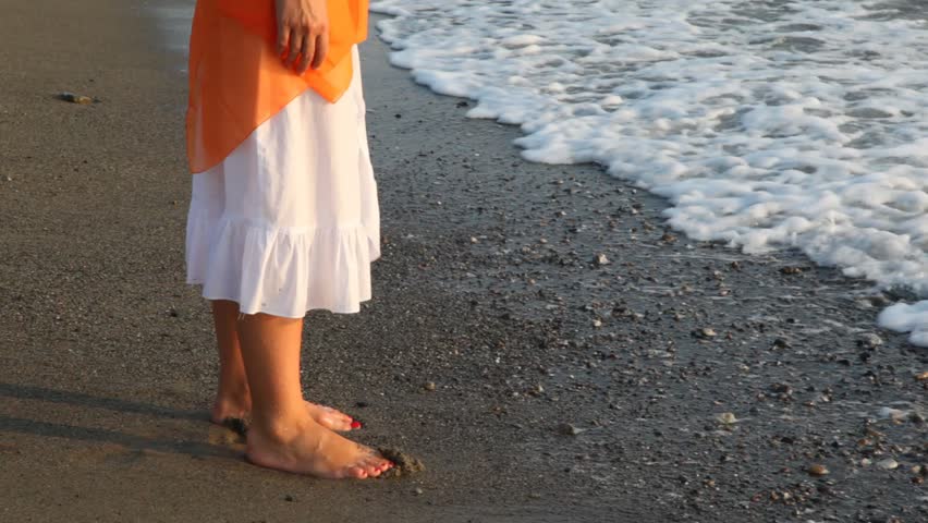 woman in white douses barefoot feet in waves of sea surf