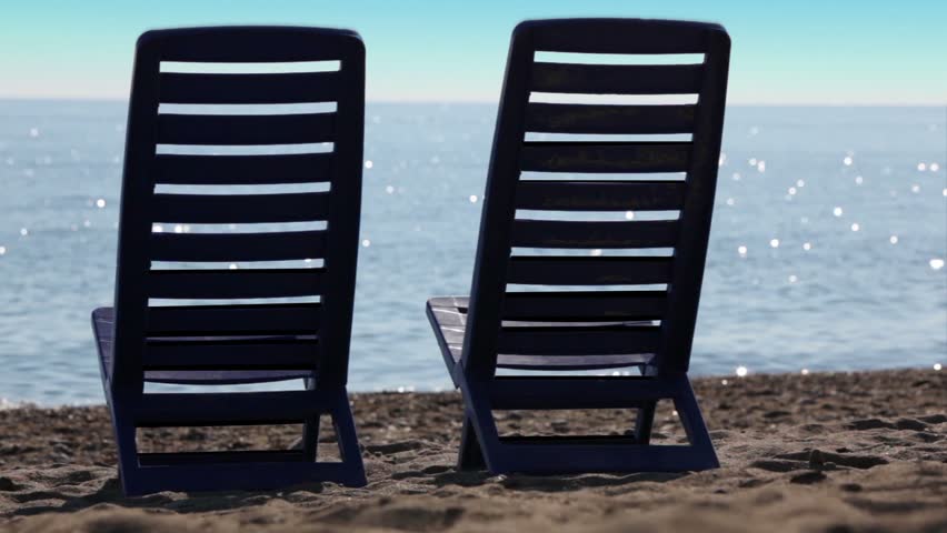Two empty deckchairs stand on beach at sunny day, camera near ground