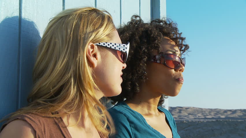 Two women friends in sunglasses blowing bubblegum at the beach