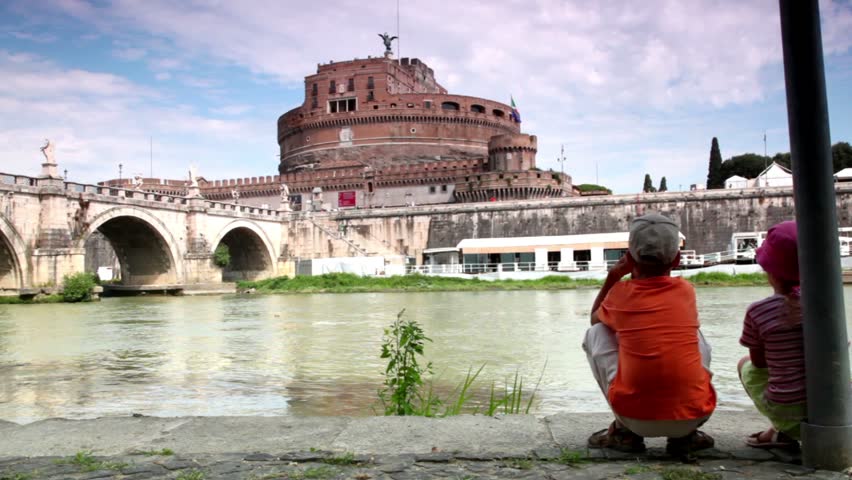 Two children brother and sister sitting on the bank of the river and look at the Sant Angelo Bridge and Sant Angelo Castel