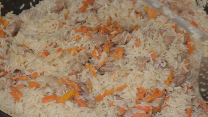 Thoroughly mixing with slotted spoon ready flavorful pilau 