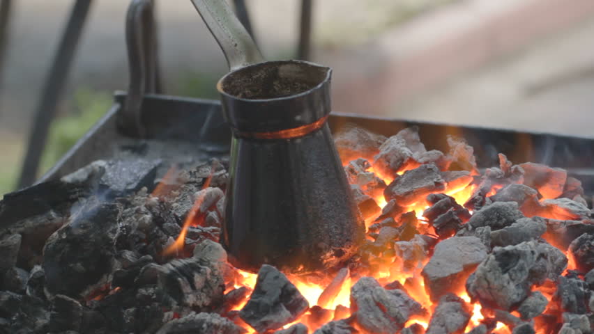 Charred pot with brewing coffee standing on fading embers 