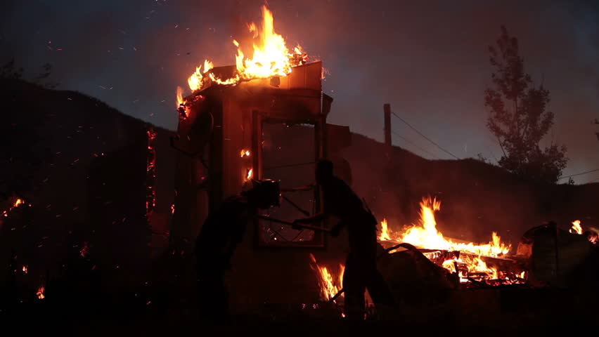 House fire during the night with flames burning and destroying the entire home. Two firemen work as silhouettes trying to control the blaze.