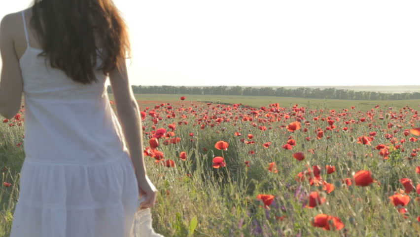 Young woman in white sundress walking through red poppies field 