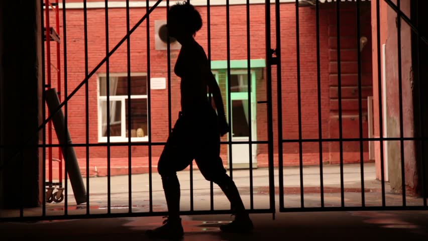 Young woman performs modern dance near lattice gate in dark lane, close-up view