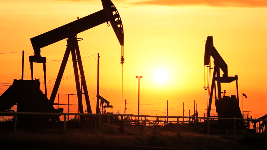 Rows of oil donkeys in silhouette at sunset in perpetual motion pumping crude oil