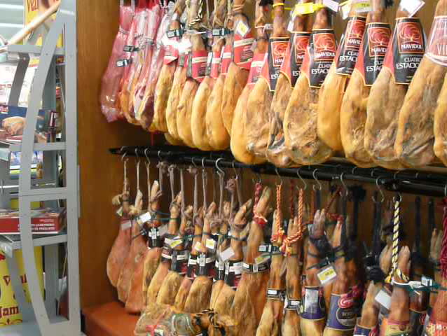 Pan across legs of cured ham hanging in a supermarket