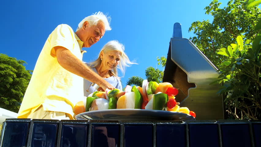 Senior couple enjoying a healthy eating lifestyle grilling delicious fresh food on a barbecue outdoors filmed at 60FPS