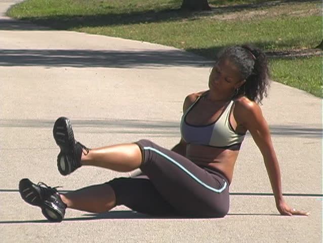 A beautiful woman stretches on a jogging track before running on a bright, sunny day.