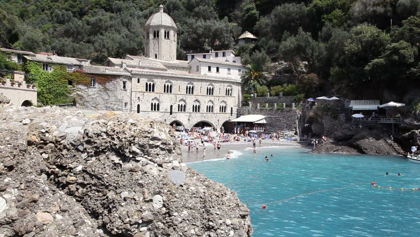 View of San Fruttuoso di Camogli, Italian Riviera, with blue sea, rocky beach and people swimming, Liguria, Italia. Two shots