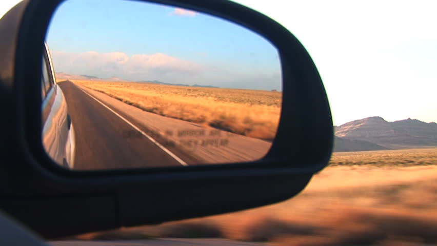 A lonely two lane blacktop flies by in a rear view mirror.