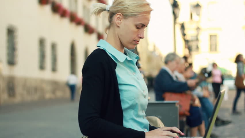 Happy businesswoman working on laptop in the city, camera stabilizer shot