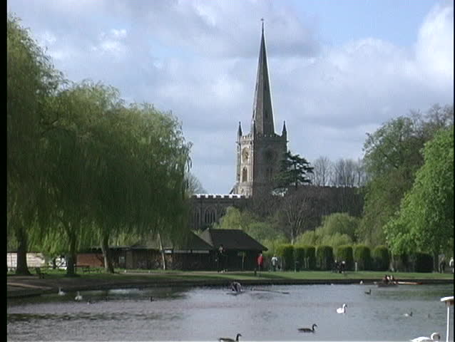 The Holy Trinity Parish Church is seen on the banks of the River Avon, while ducks swim in the gentle river current.