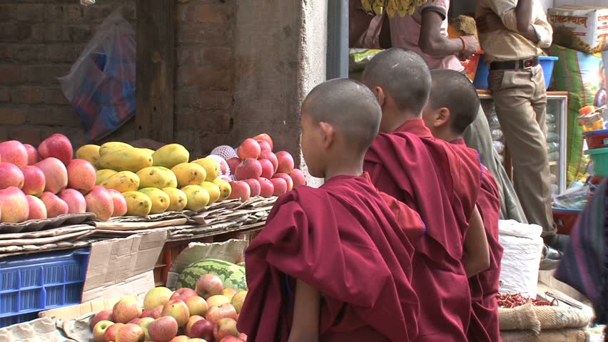 Three young buddhist monks stand in front of a fruit stand