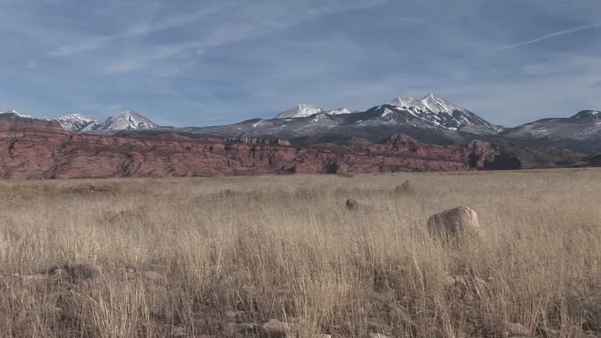 Snow-capped mountains rise above grassy plains of the American Southwest desert.