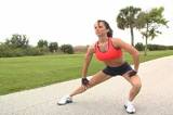 A pretty brunette in fitness wear, with remarkable muscle definition, stretches prior to jogging outdoors.  Low angle.