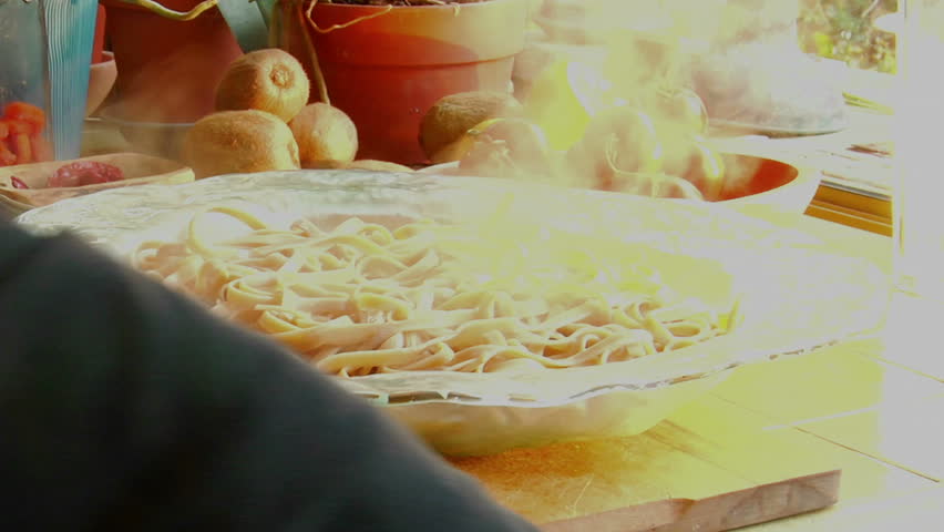 A woman chef prepares a meal by pouring fresh cooked sauce onto a steaming bowl of pasta