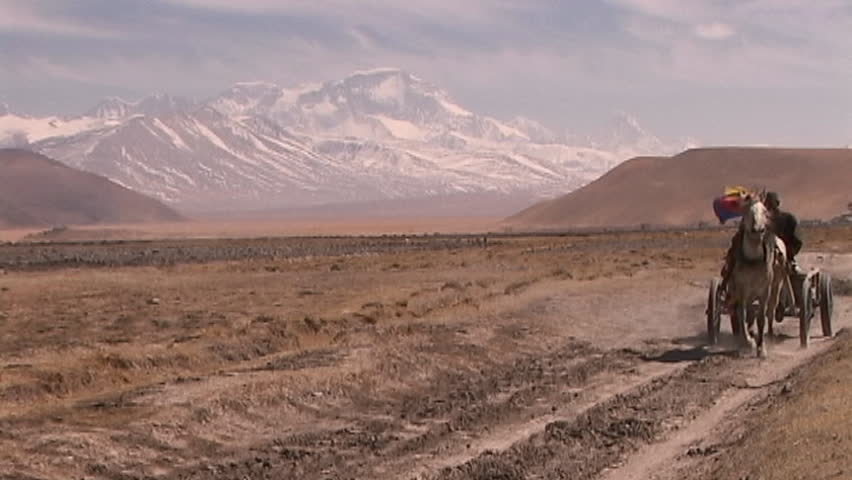 Tibetan man riding in carriage pulled by horse across the Tibetan Plateau with Mt. Cho Oyu in the background