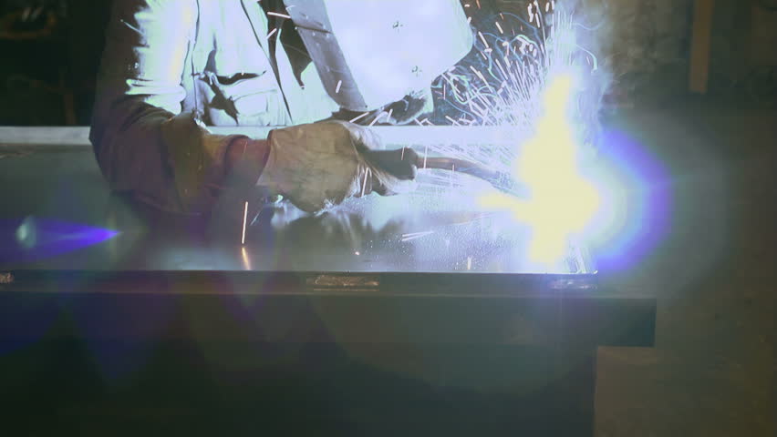 Welder in steel factory employed as manual worker with protective mask, tools and machine on iron