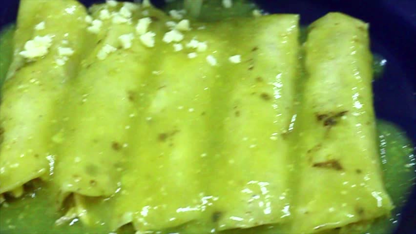 finishing enchiladas with green sauce and cheese