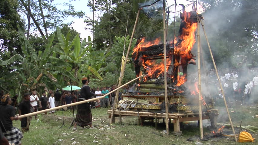 BALI, INDONESIA - CIRCA 2009: Men use long poles to poke at a funeral pyre during a cremation ceremony in Bali.