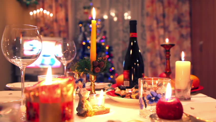 Decorated christmas dining table with bottle, glasses, candy, candles, christmas tree and tvset in background