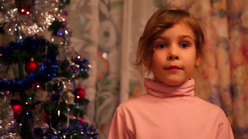 Girl stand near decorated christmas tree and says her wishes, when she tells verse