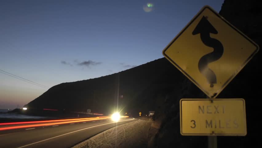 A time lapse shot of traffic at night passing a roadsign.