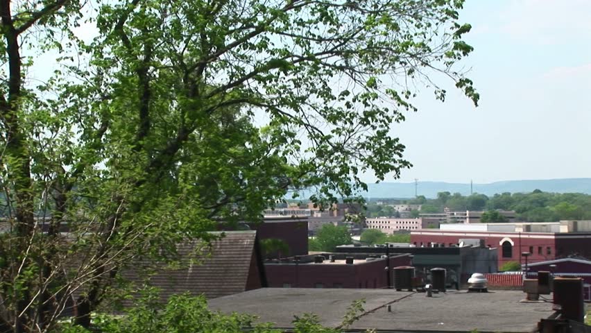 The camera pans-right across the roofline of a small town to highlight an old clock tower.