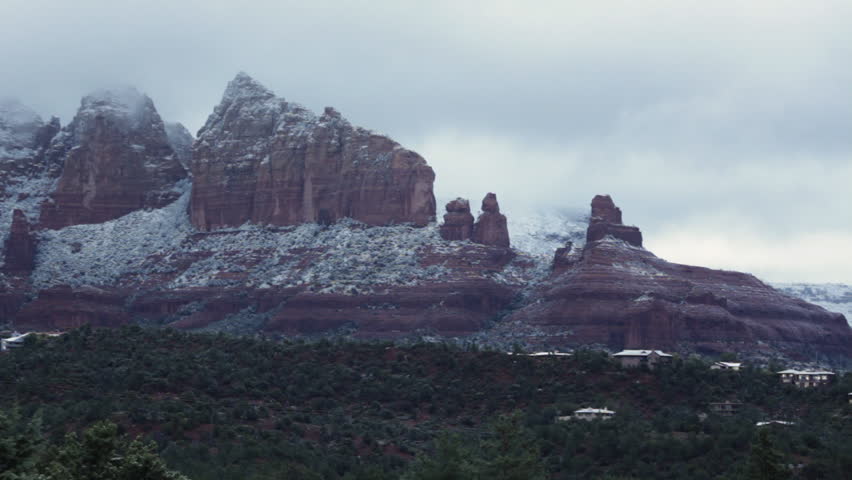A wide shot of rock formations and slow-moving clouds in Sedona, Arizona covered under a light dusting of the first snow of the season.