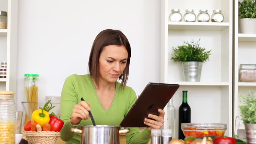 Woman in kitchen looking at recipe on tablet computer 