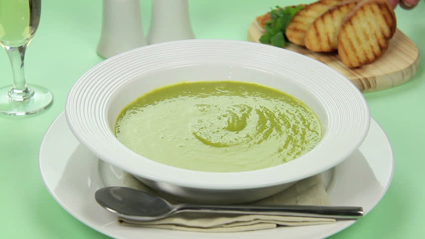 Crunchy piece of grilled bread being dipped into a bowl of pea soup
